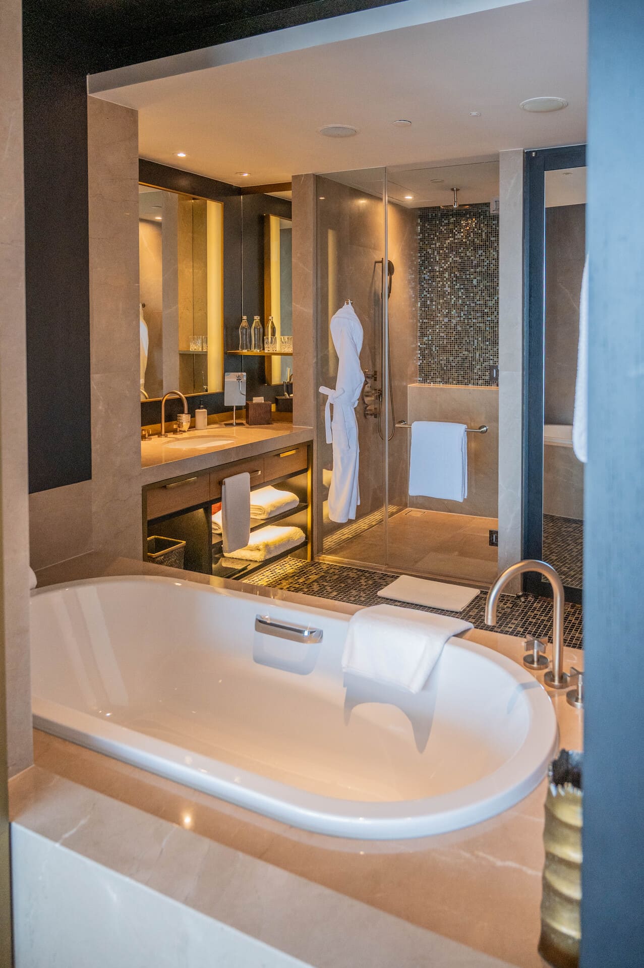 Modern luxury bathroom at the Rosewood Phnom Penh in Cambodia, with an oval soaking bathtub, illuminated vanity, and glass walk-in shower